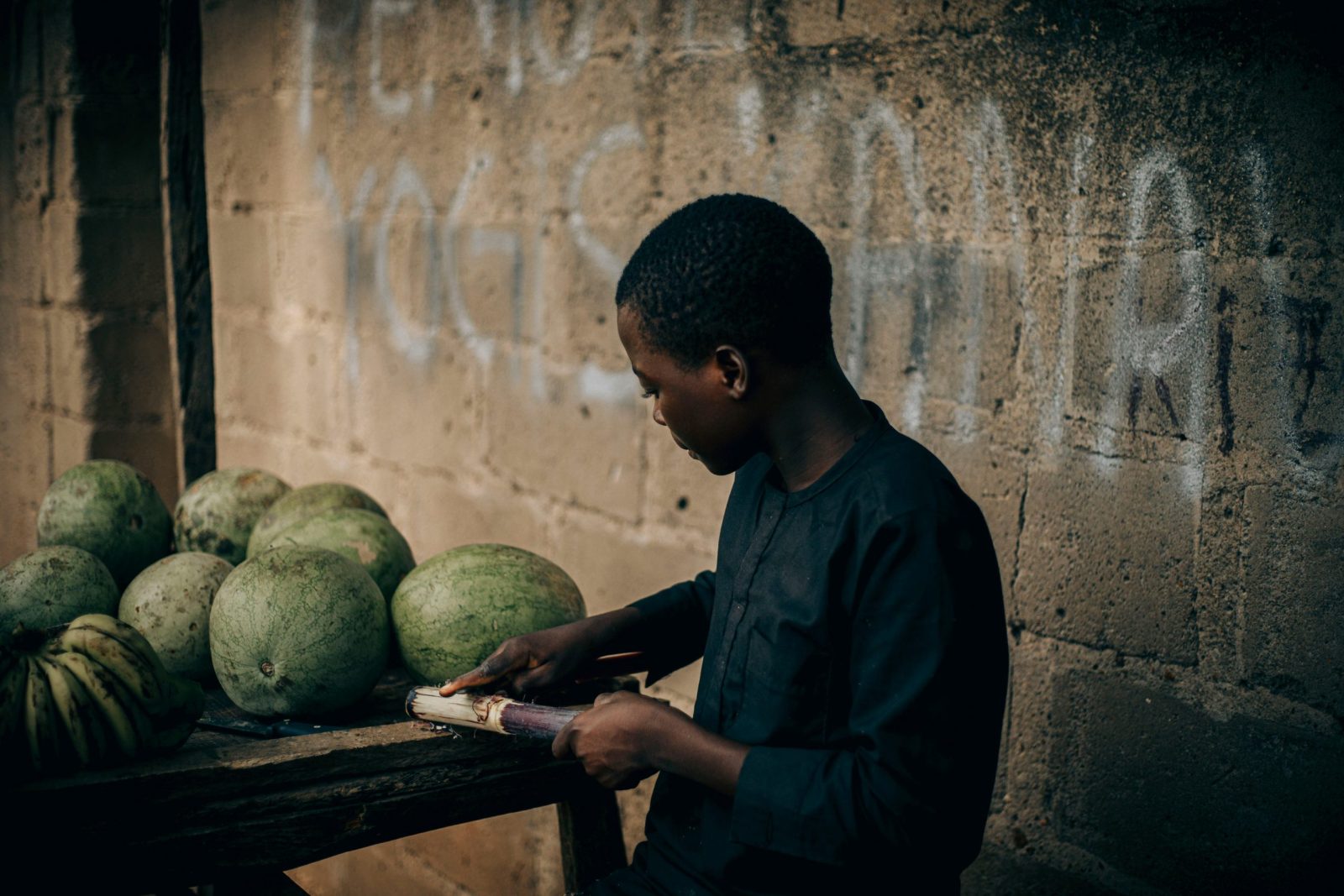 A boy cutting sugarcane beside a table of produce in Yobe, Nigeria.